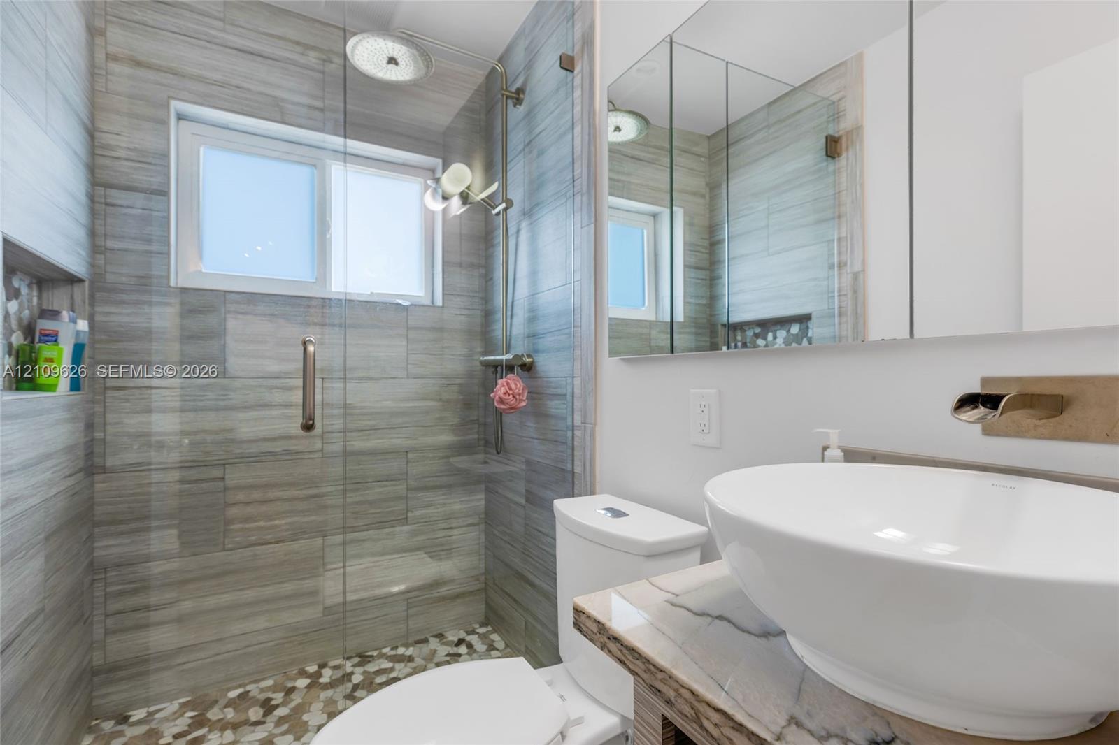 Bathroom featuring a walk-in shower with large-format horizontal tile, pebble-stone flooring, rainfall showerhead, and a glass partition