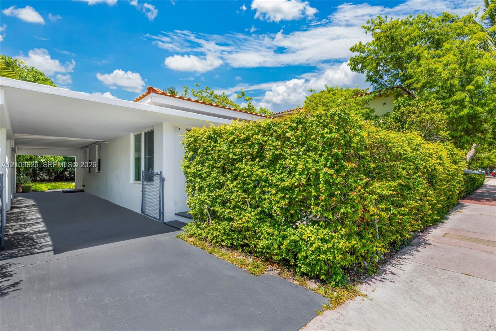 White stucco exterior featuring a flat roofline, integrated carport, and mature perimeter landscaping