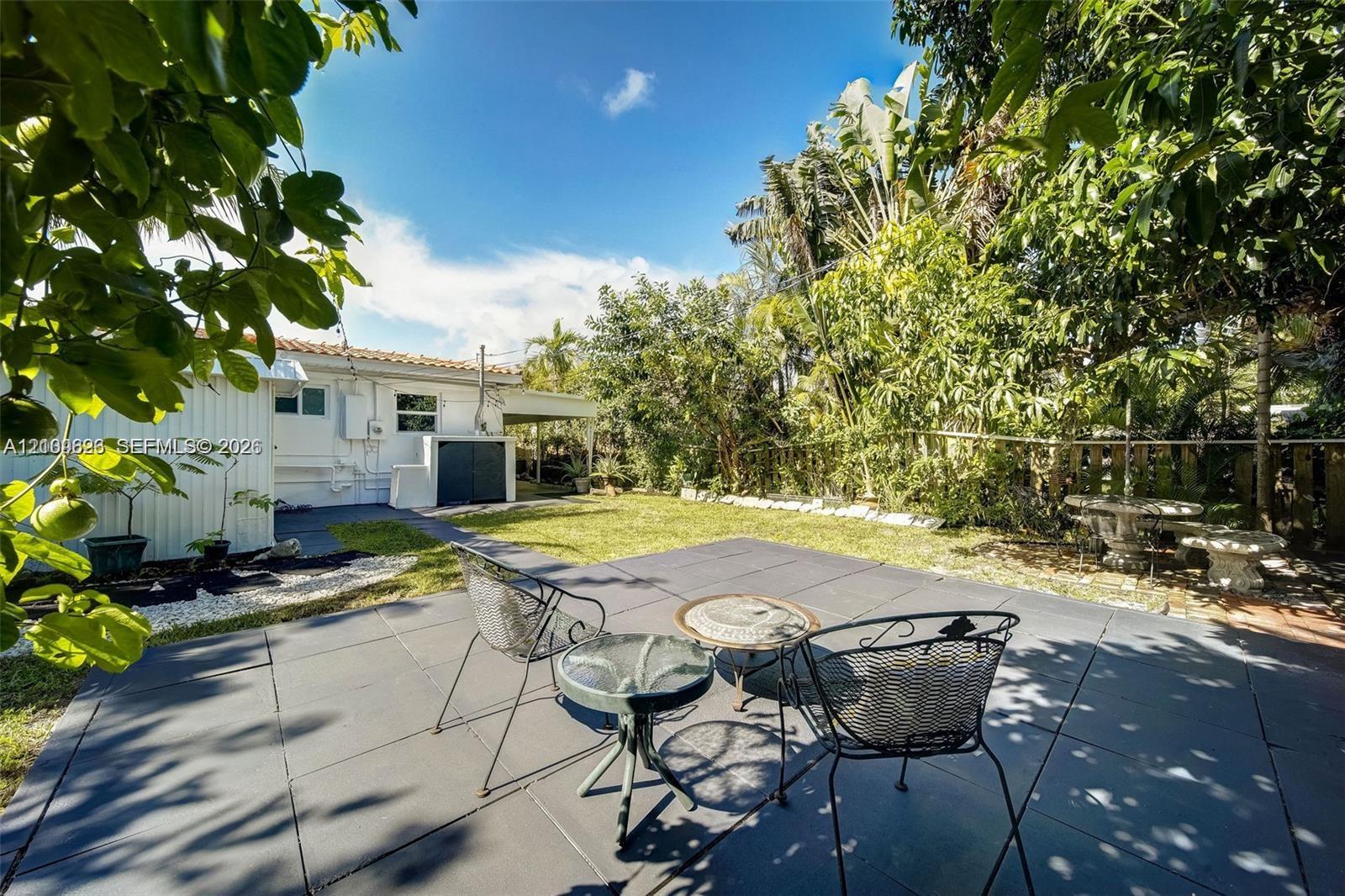 Rear yard featuring a dark-tiled patio, manicured lawn, established landscaping, and a white exterior wall