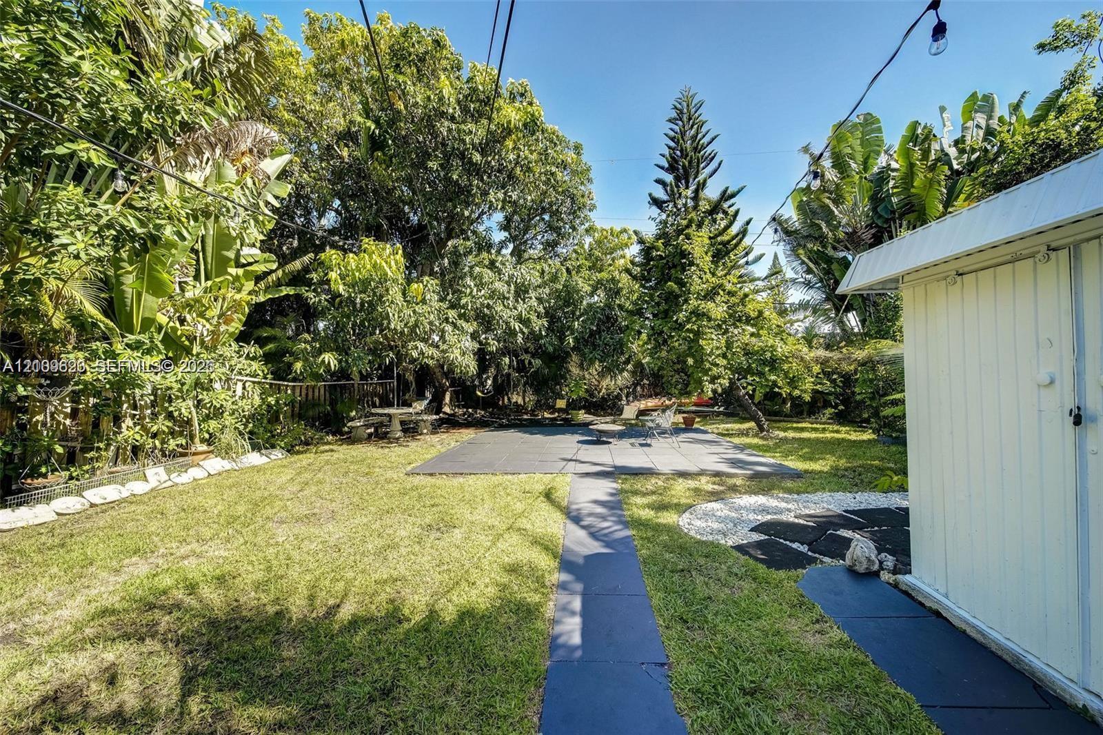 Private backyard featuring a grass lawn, paved patio area, mature perimeter trees, and a detached exterior storage structure