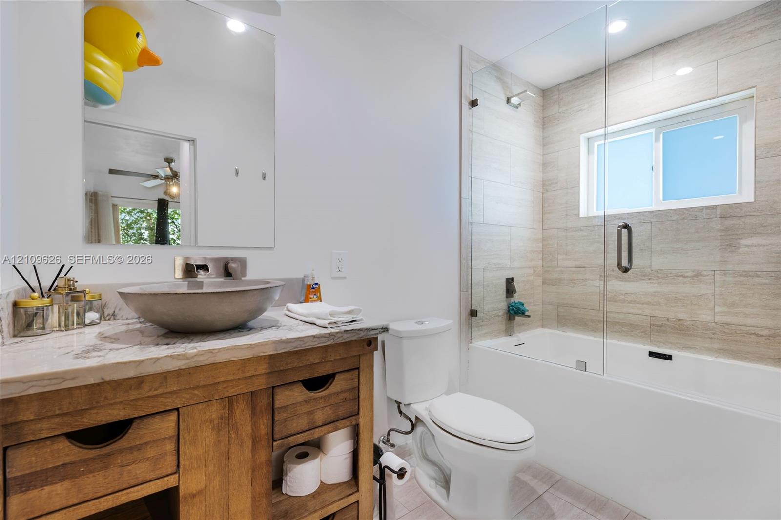 Bathroom featuring a wood-finish vanity with stone countertop, vessel sink, wall-mounted faucet, and a tiled shower enclosure with a glass panel