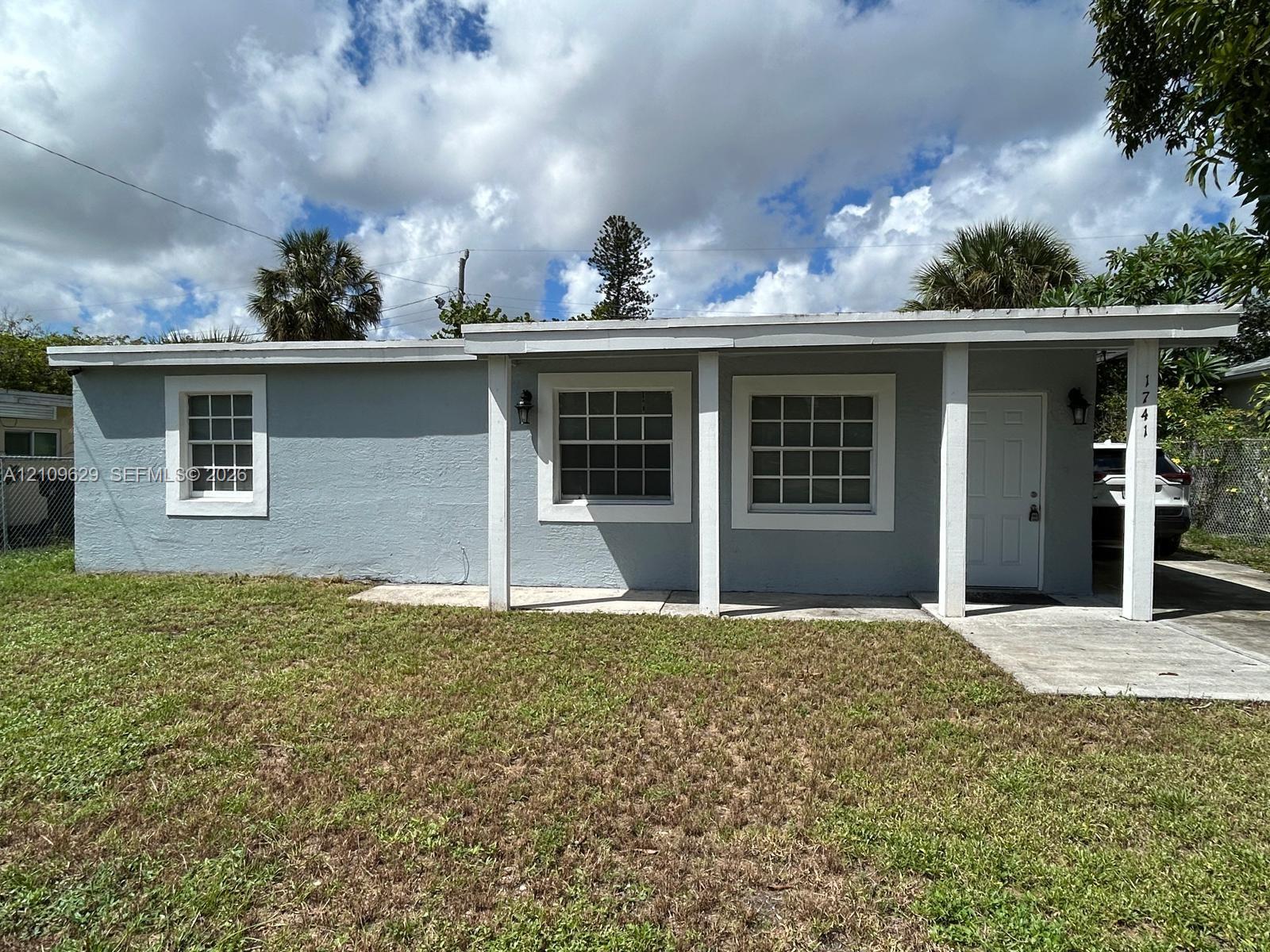 Single-story exterior featuring light gray stucco siding, a covered front porch, square-grid windows, and a concrete driveway