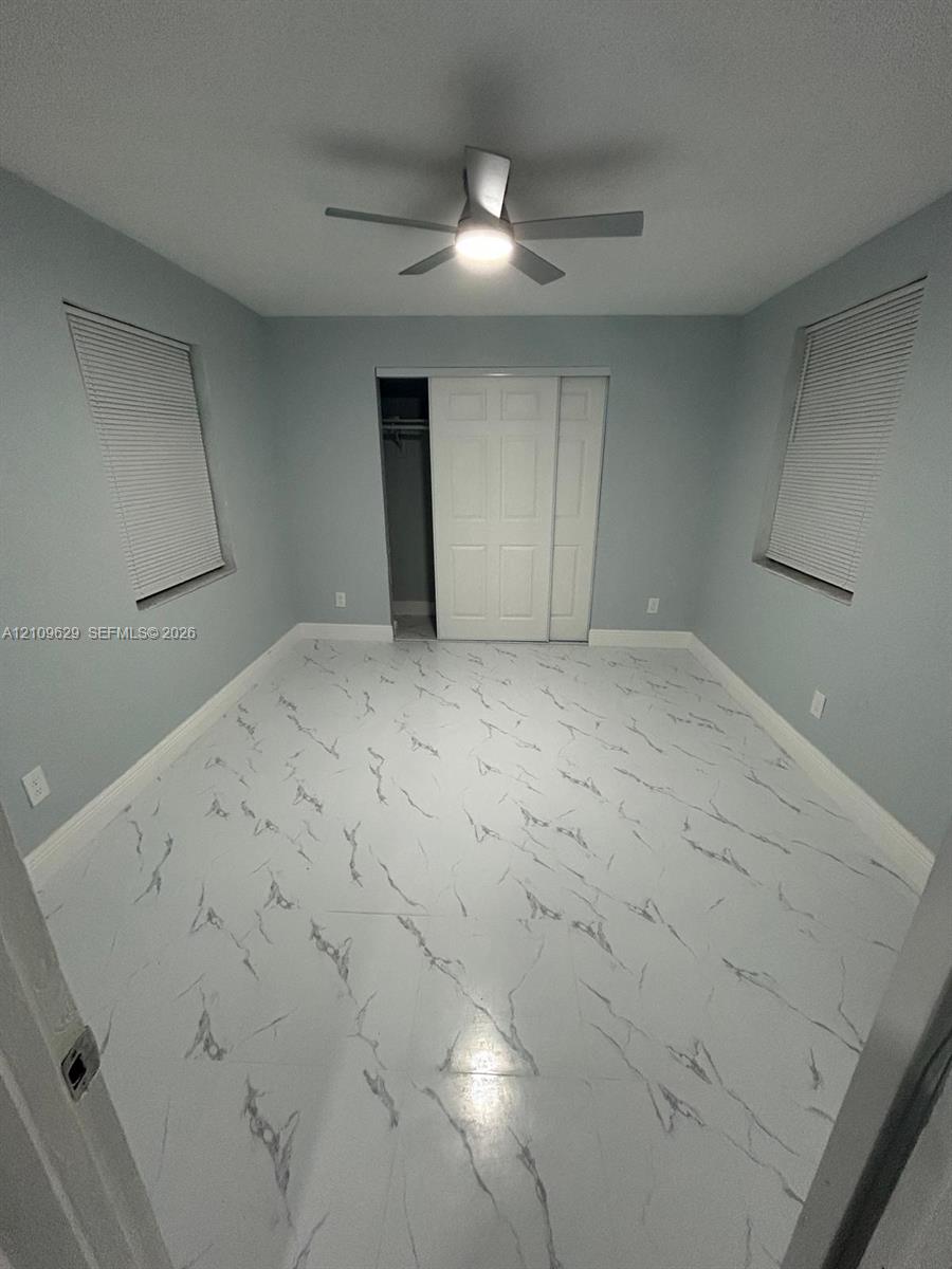 Interior space featuring light-toned, high-contrast patterned flooring, dual windows with integrated blinds, a ceiling fan with integrated lighting, and a closet with sliding paneled doors