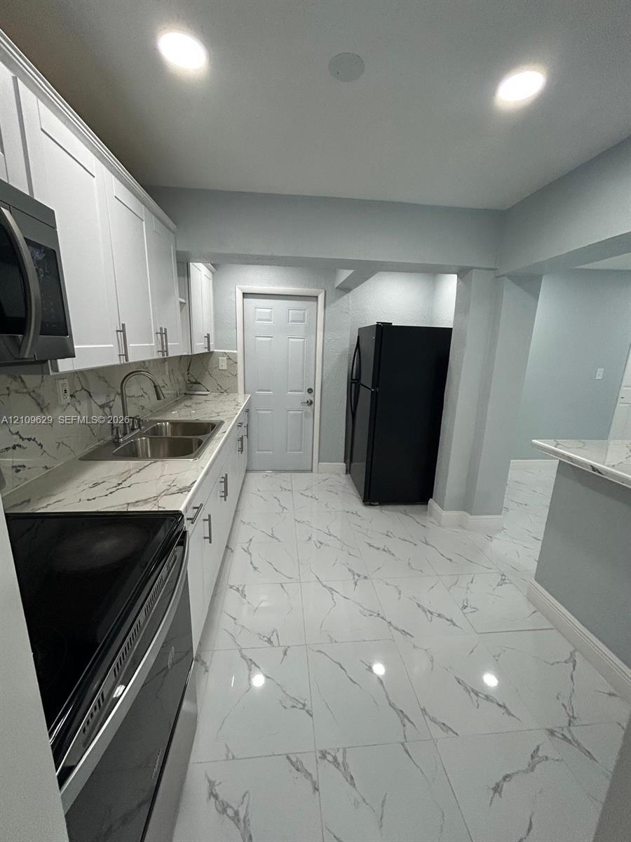 Kitchen featuring white shaker-style cabinetry, stone-patterned countertops, large-format tiled flooring, recessed lighting, and integrated stainless steel microwave