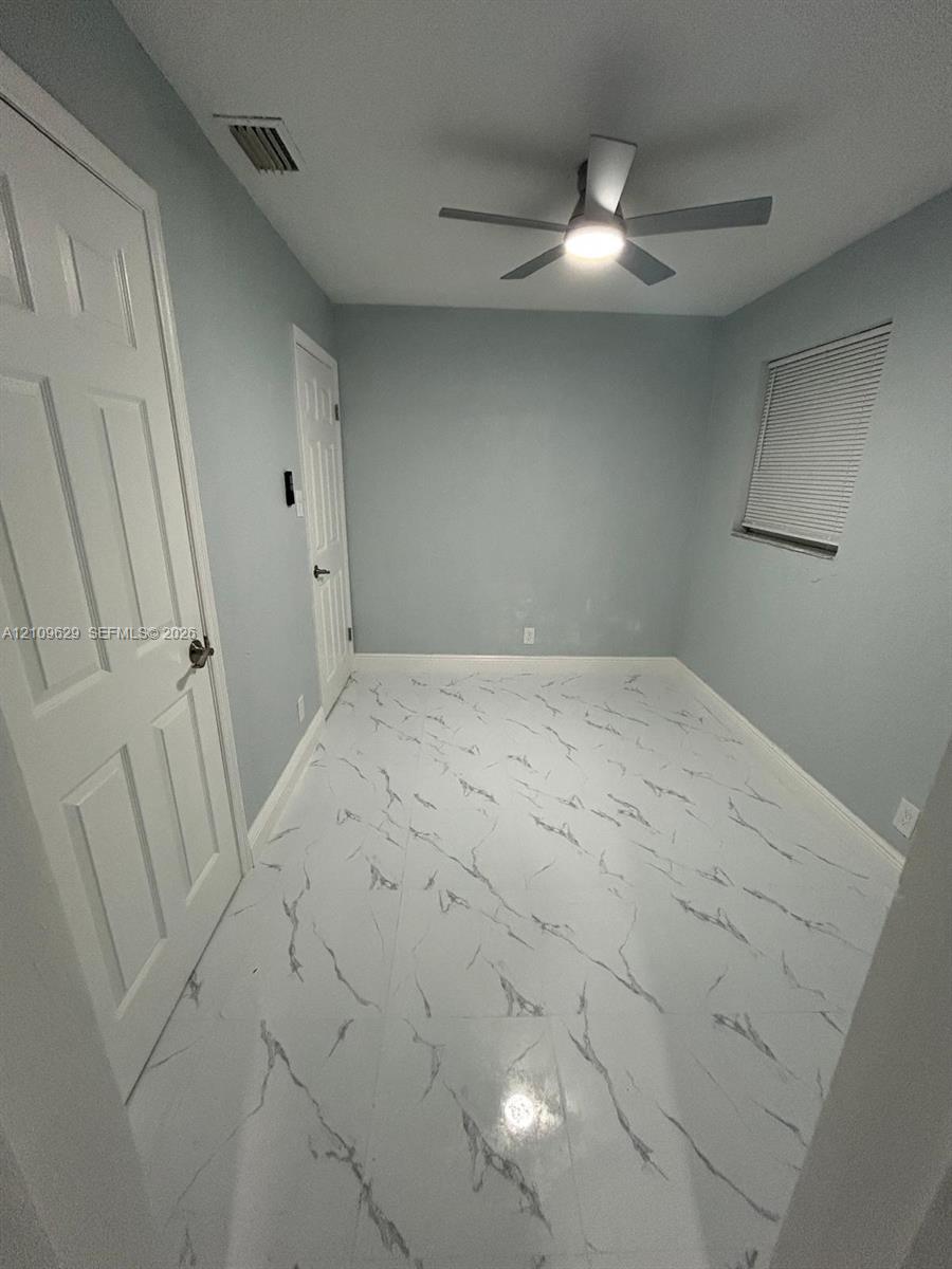 Room featuring polished, marble-patterned tile flooring, neutral wall paint, white six-panel interior doors, and a ceiling-mounted light fixture with integrated fan
