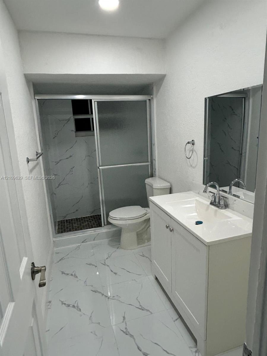 Bathroom featuring white cabinetry with integrated countertop, polished large-format tile flooring, shower enclosure with glass doors, and decorative wall tiling