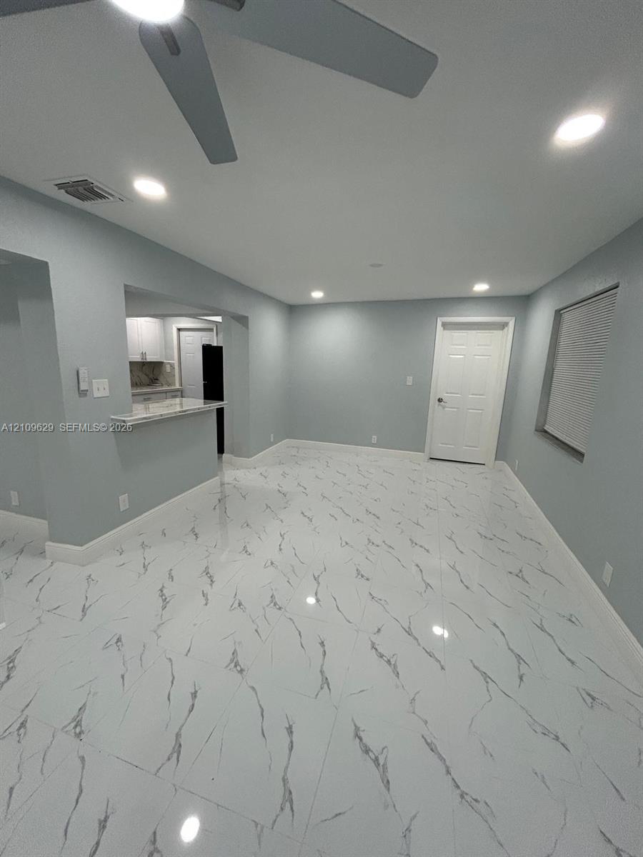 Polished tile flooring with high-contrast veining, recessed lighting, ceiling fan, and a pass-through breakfast bar featuring stone-surface countertop