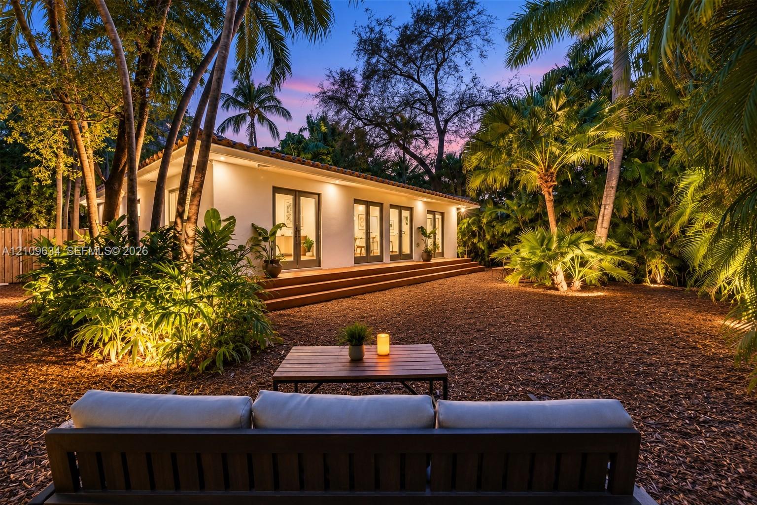 Stucco exterior featuring multiple sets of French doors, a tiered wood-finish deck, and mature tropical landscaping