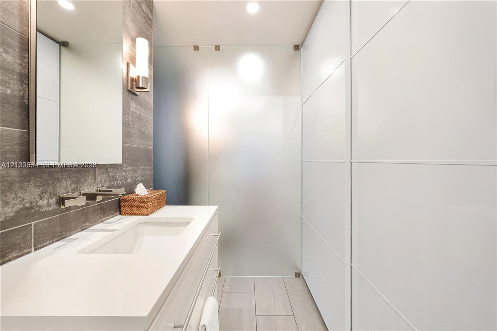 Modern vanity with integrated rectangular sink, wall-mounted faucet, stone-textured tile wall, and glass panel shower enclosure