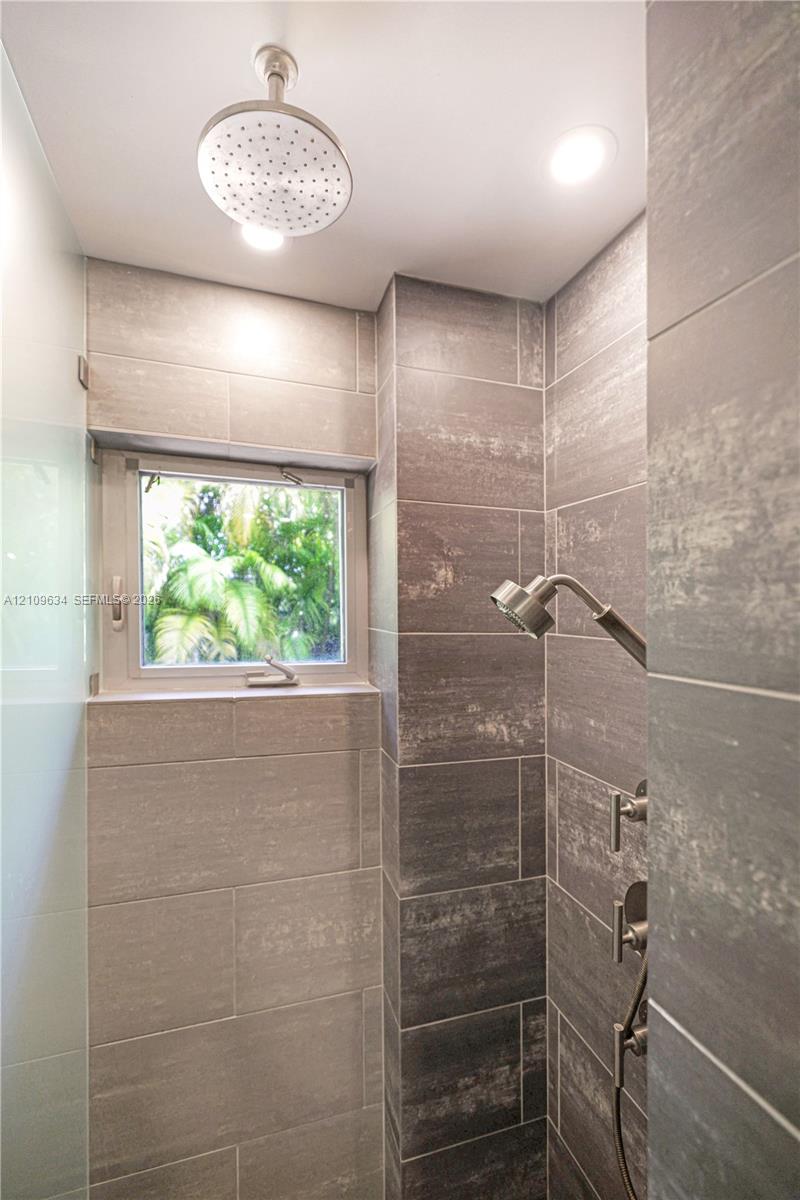 Shower enclosure featuring floor-to-ceiling large-format tile, ceiling-mounted rainfall showerhead, adjustable handheld shower fixture, and built-in window