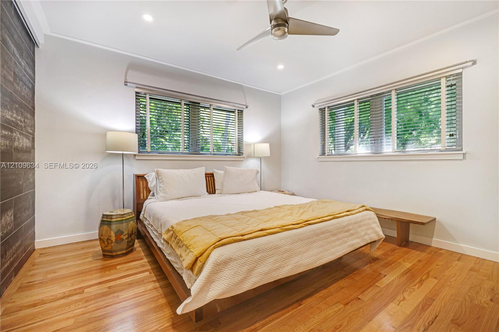 Hardwood flooring, accent wall with tile finish, dual windows with horizontal blinds, and ceiling fan