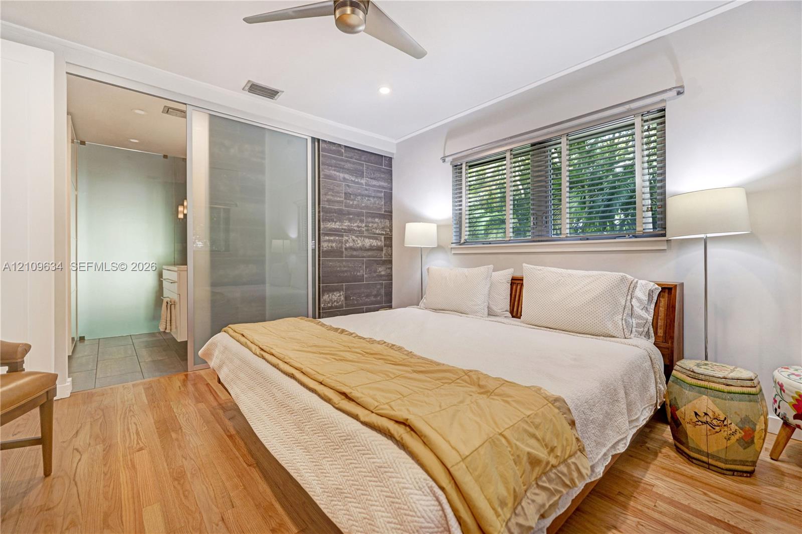 Wood-finish flooring, sliding frosted glass door, horizontal slat-textured accent wall, and ceiling fan