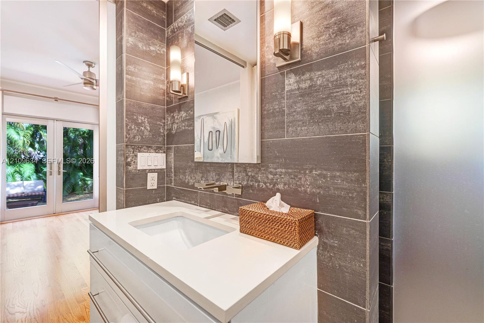Modern vanity featuring a white rectangular sink, quartz countertop, and wall-mounted faucet, complemented by large-format textured tile wall cladding and integrated vertical light fixtures