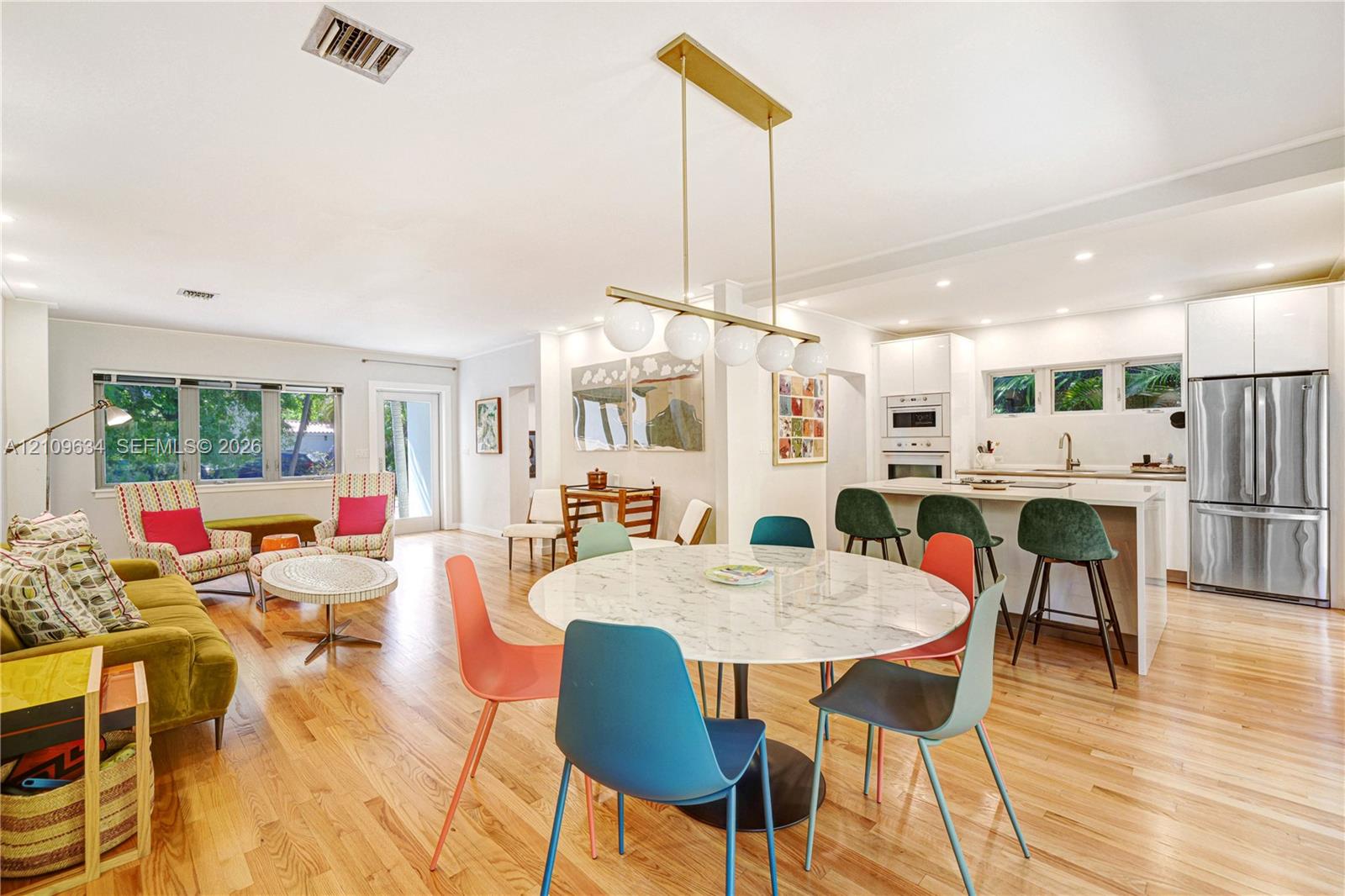 Open-concept layout featuring wood-finish flooring, a kitchen island with quartz-style countertop, stainless steel refrigerator, and modern globe pendant lighting