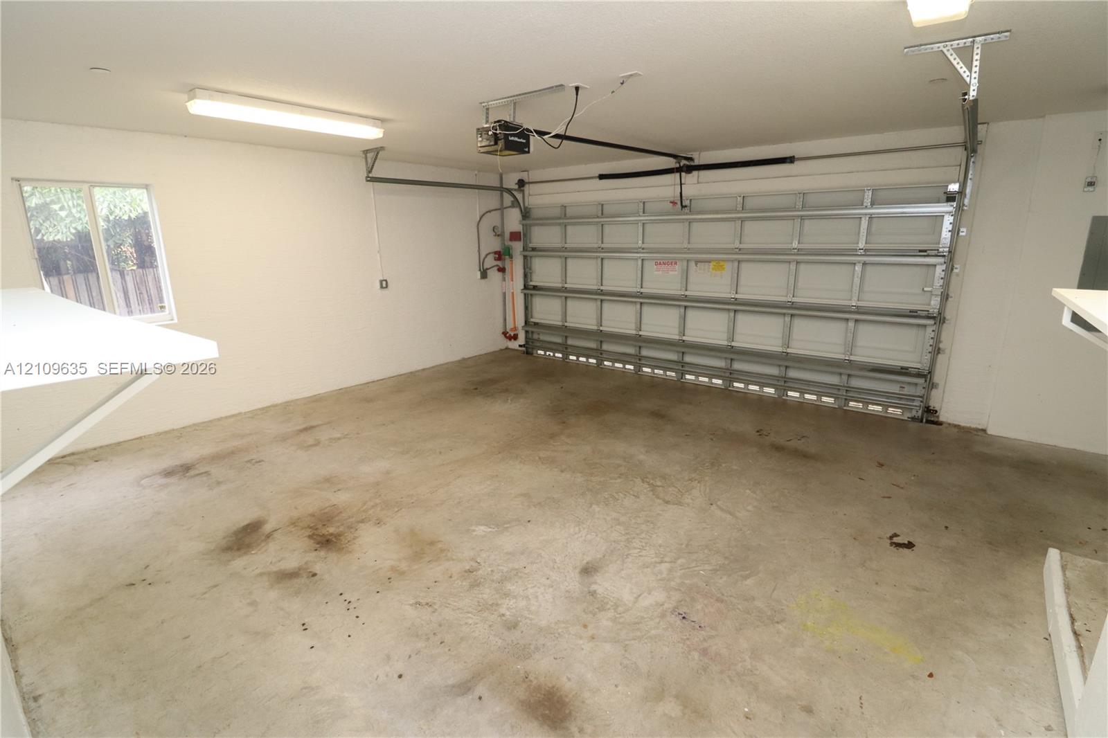 Two-car garage featuring a sectional metal roll-up door, concrete flooring, overhead linear lighting, and a window