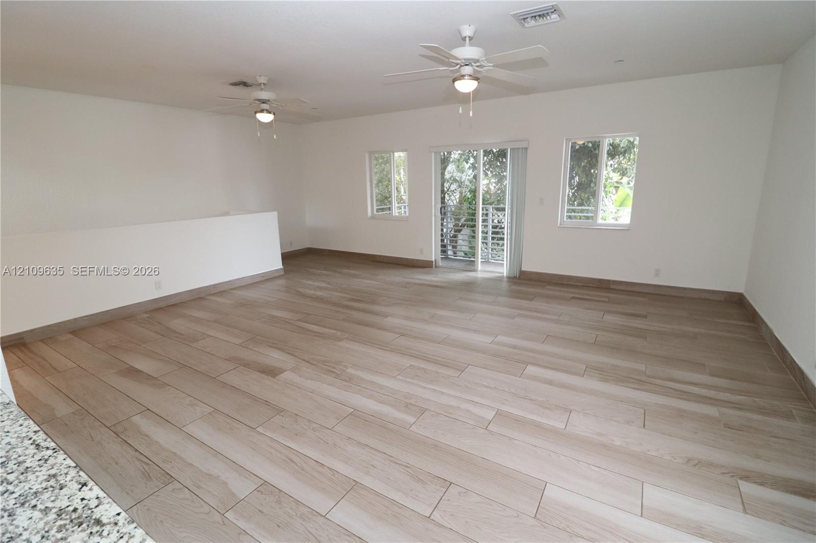 Open-concept interior featuring light wood-finish flooring, dual ceiling fans, sliding glass doors, and large windows