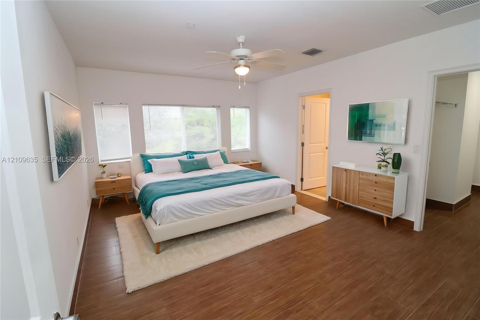 Bedroom featuring wood-finish tile flooring, three paneled windows, and a central ceiling fan with integrated lighting