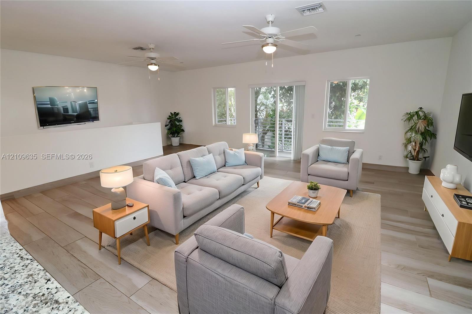 Open-concept interior featuring wood-finish flooring, recessed ceiling lighting, dual ceiling fans, and sliding glass doors with exterior access