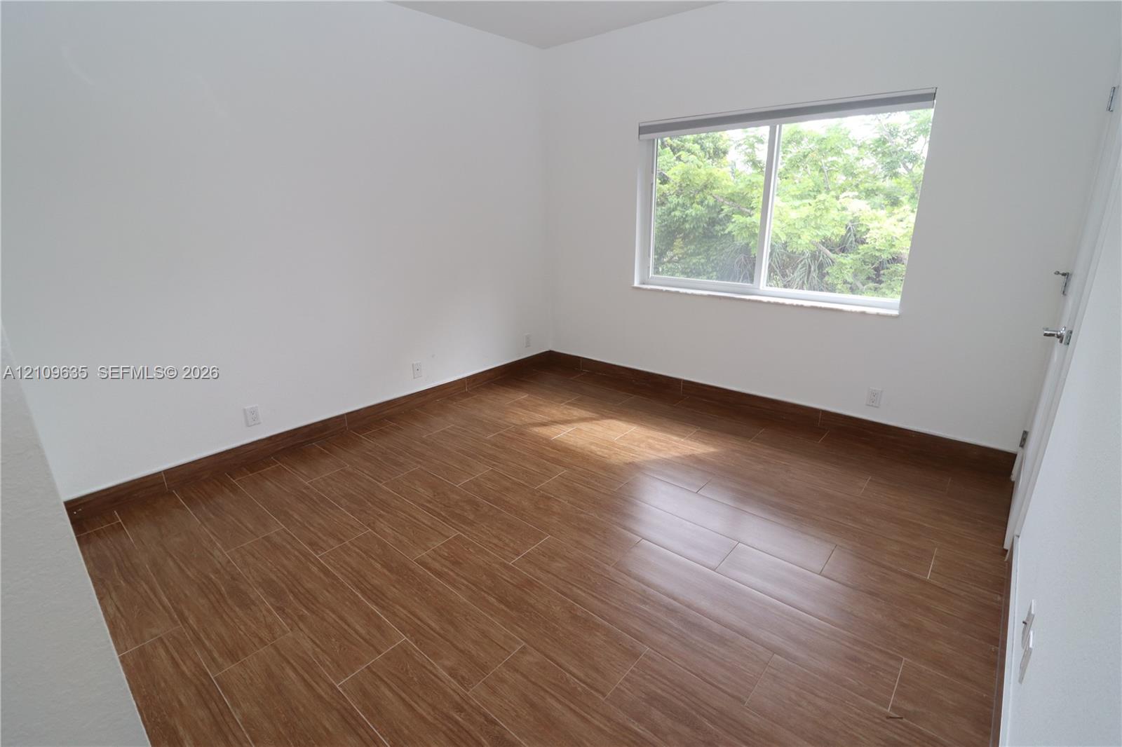 Neutral wall tones, wood-finish flooring, and a large window featuring horizontal blinds