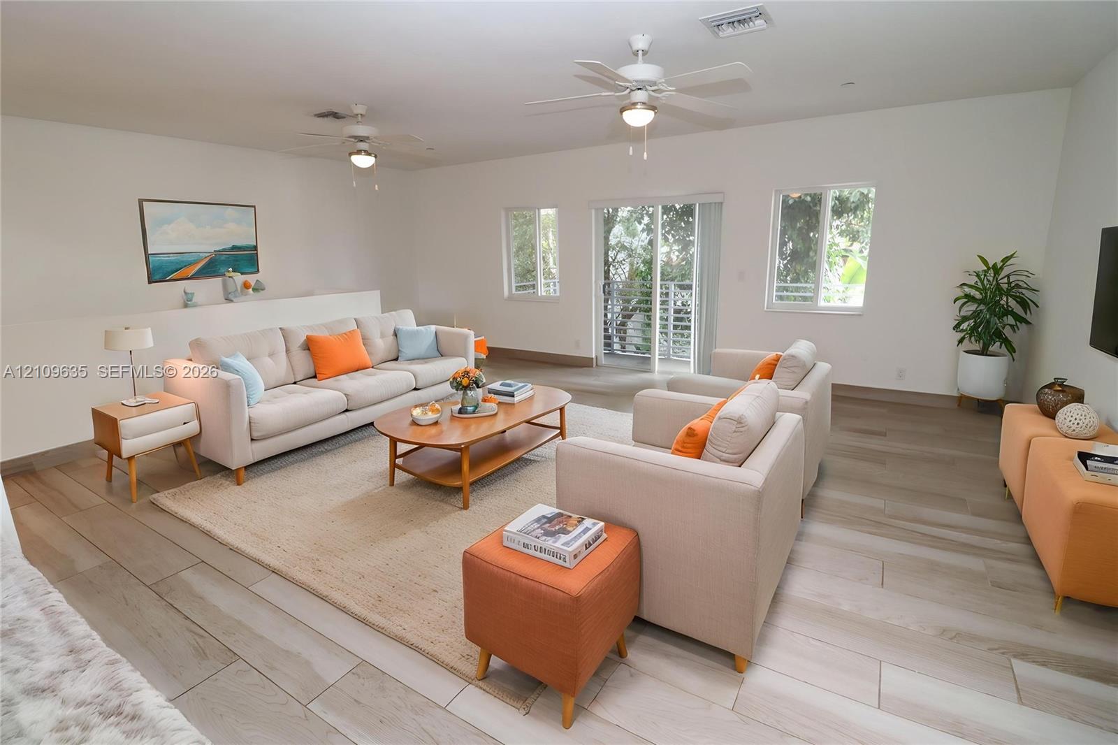 Living area featuring light-toned wood-finish flooring, dual ceiling fans, multiple windows, and sliding glass doors with balcony access