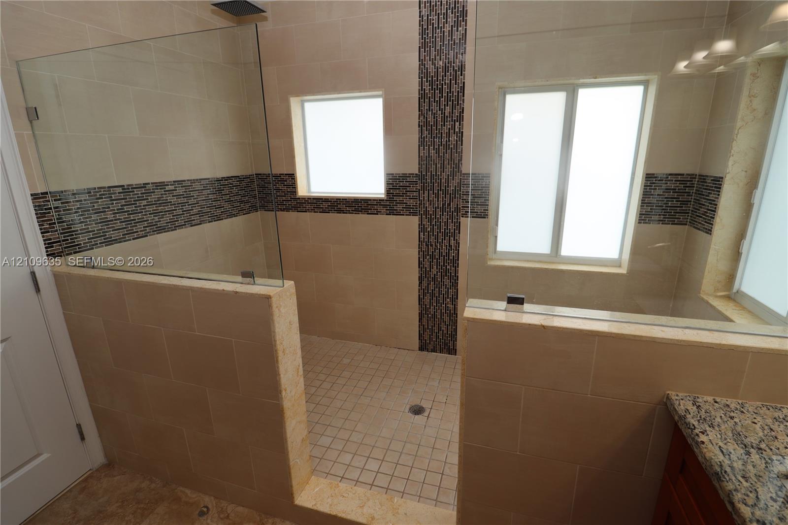 Walk-in shower featuring large-format stone-look tile walls, decorative mosaic accent banding, a glass enclosure, and stone-look tile flooring