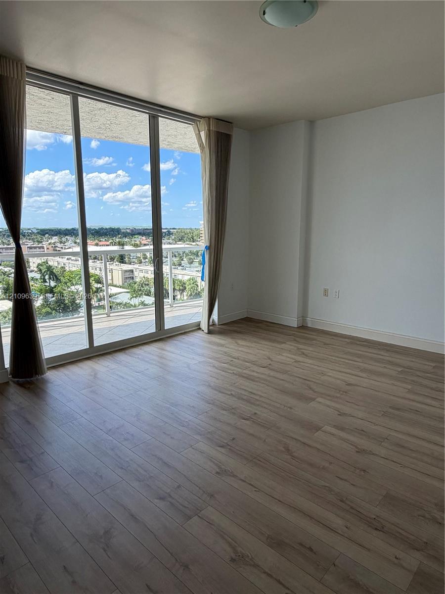 Floor-to-ceiling glass sliding doors, wood-finish flooring, and a private balcony with a glass railing