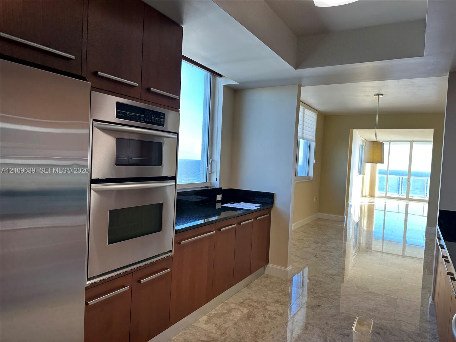 Kitchen featuring stainless steel double wall ovens, dark cabinetry, polished stone countertops, and stone flooring