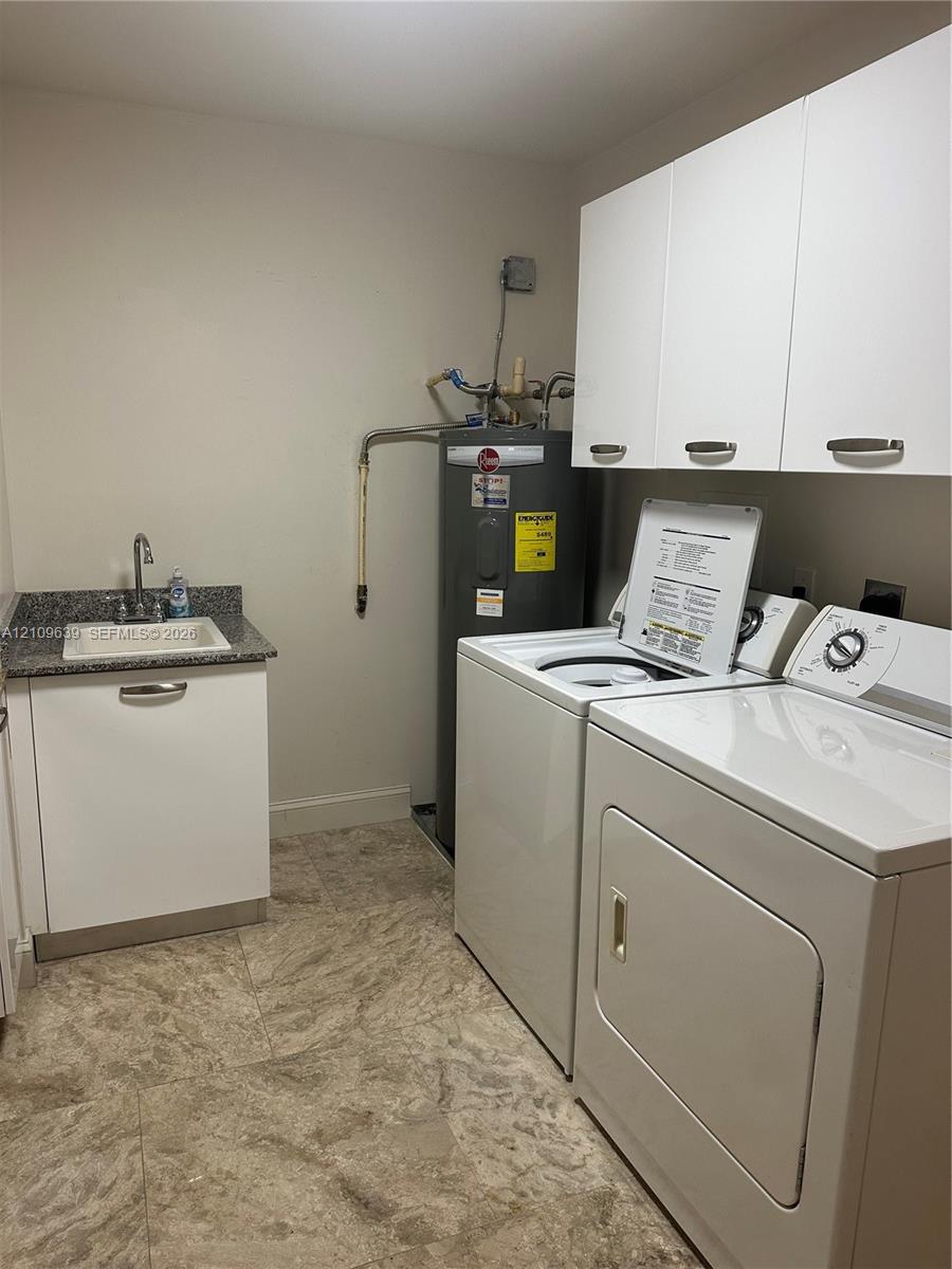 Utility area featuring stone-finish flooring, white cabinetry, a sink with a stone-top counter, and a vertical water heater