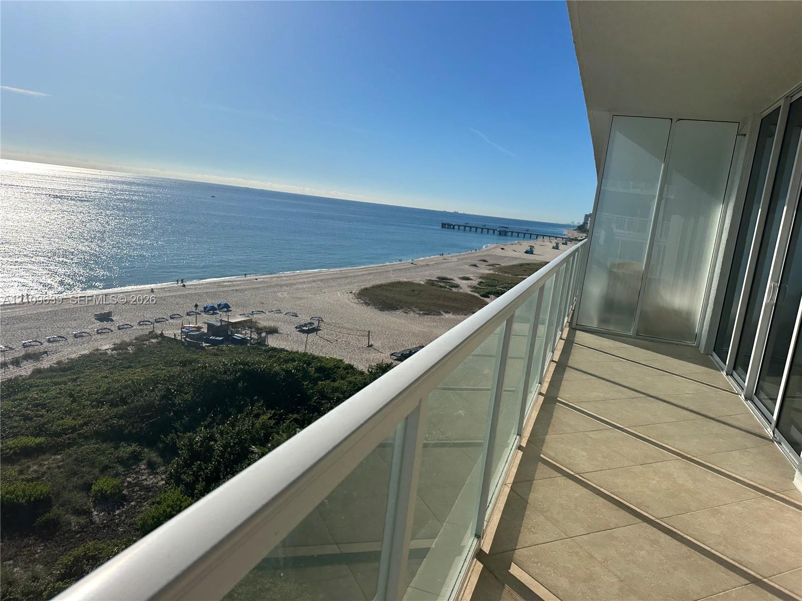 Covered balcony featuring tile flooring, glass panel railings, and oceanfront scenery