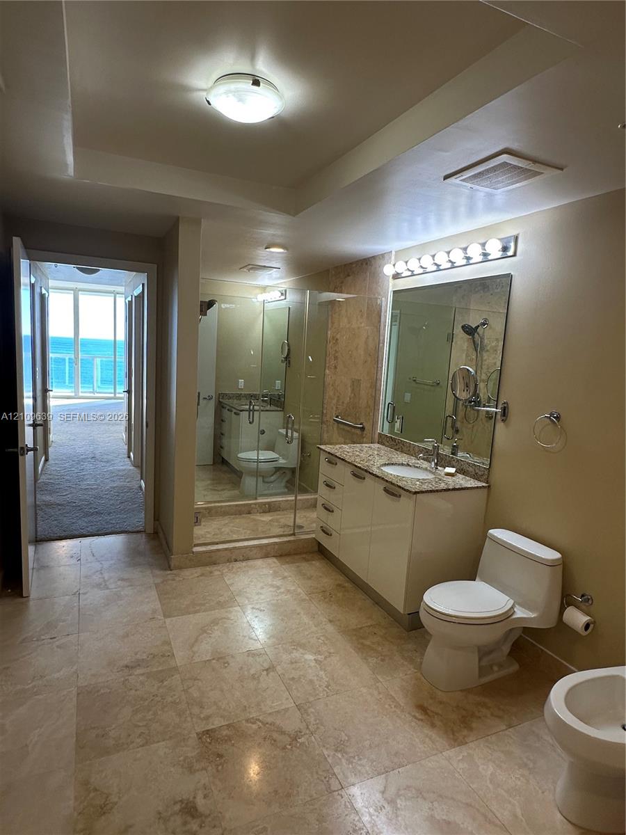 Hi & Hers Bathroom featuring large-format stone flooring, vanity with stone countertop and undermount sink, glass-enclosed shower, and wall-mounted light fixtures