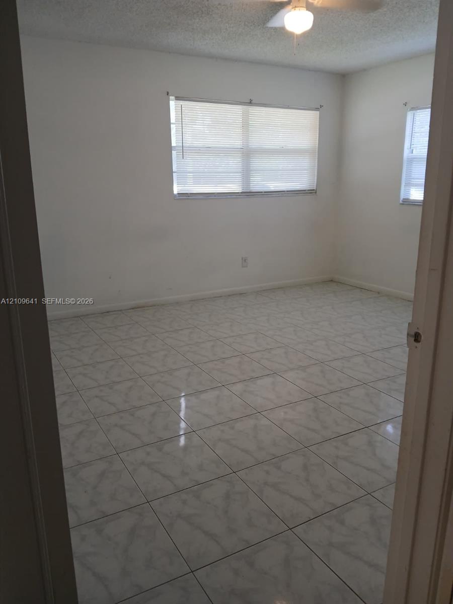 Interior room featuring neutral wall-to-wall ceramic tile flooring, dual windows, and an attached ceiling fan with light fixture Interior room featuring neutral wall-to-wall ceramic tile flooring, dual windows, and an attached ceiling fan with light fixture