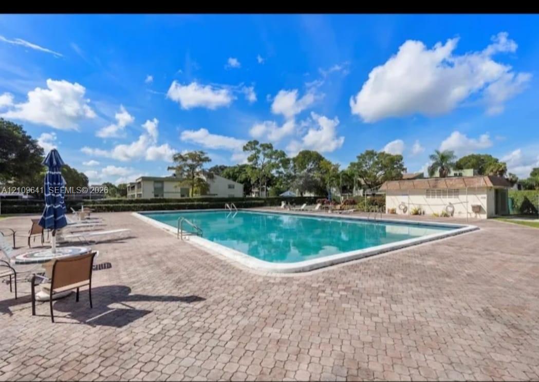 Rectangular swimming pool featuring a brick paver deck, metal safety handrails, and a nearby utility structure Rectangular swimming pool featuring a brick paver deck, metal safety handrails, and a nearby utility structure