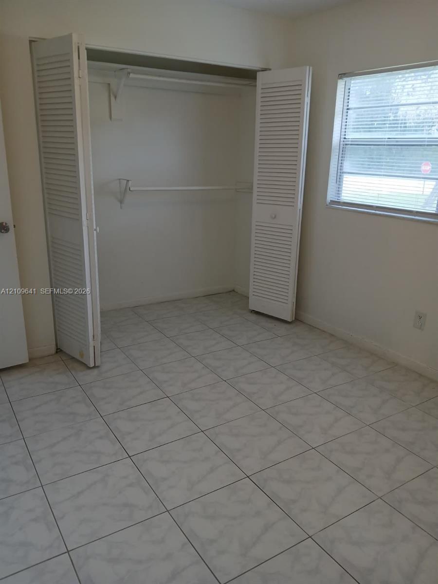 Square-tile flooring, louvered bi-fold closet doors, and single-hung window featuring horizontal blinds