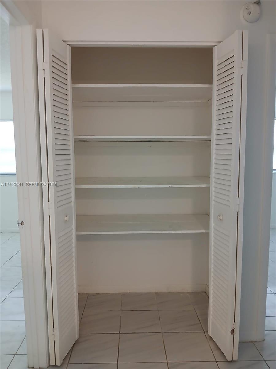 Storage closet featuring dual white louvered doors and three built-in shelves