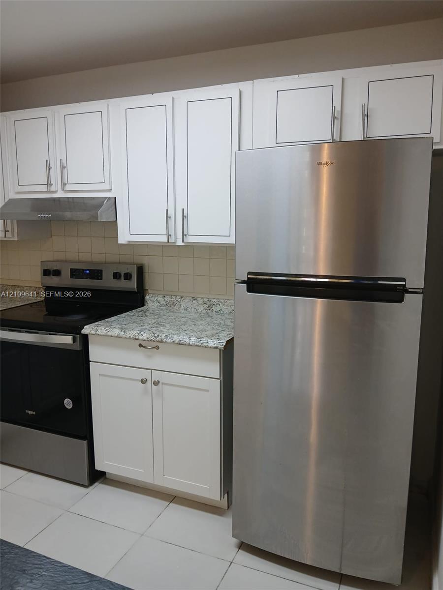 Kitchen featuring white shaker-style cabinetry, stone-finish countertops, stainless steel appliances, and a square-tile backsplash Kitchen featuring white shaker-style cabinetry, stone-finish countertops, stainless steel appliances, and a square-tile backsplash