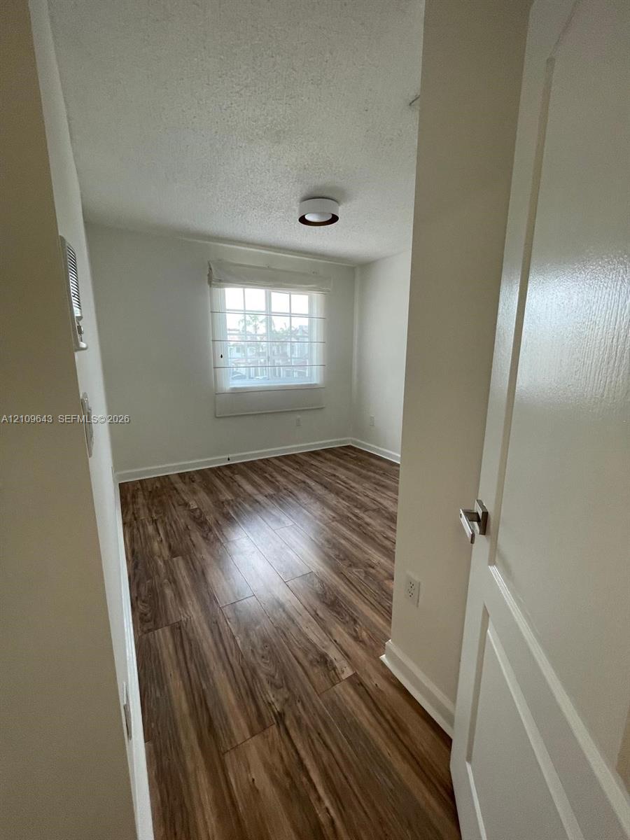 Room featuring wood-finish flooring, a multi-pane window with a built-in blind, and a central flush-mount ceiling light fixture
