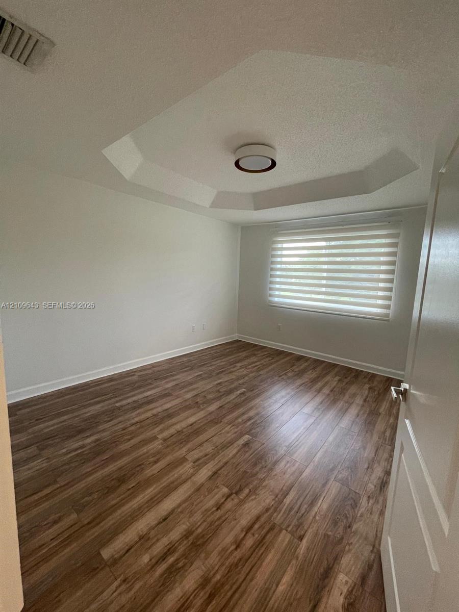Interior space featuring wood-finish flooring, a tray ceiling, flush-mount lighting, and a window with installed roller shades