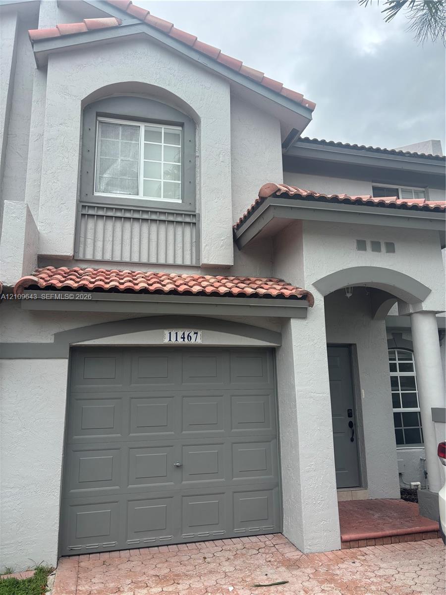 Stucco exterior featuring terracotta-style roof tiles, arched architectural detailing, a paneled garage door, and a covered entryway with column support Stucco exterior featuring terracotta-style roof tiles, arched architectural detailing, a paneled garage door, and a covered entryway with column support