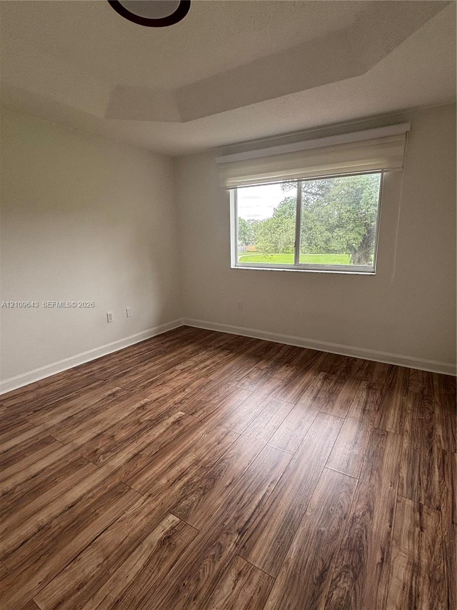 Tray ceiling, wood-finish flooring, and single-pane window with a roller shade