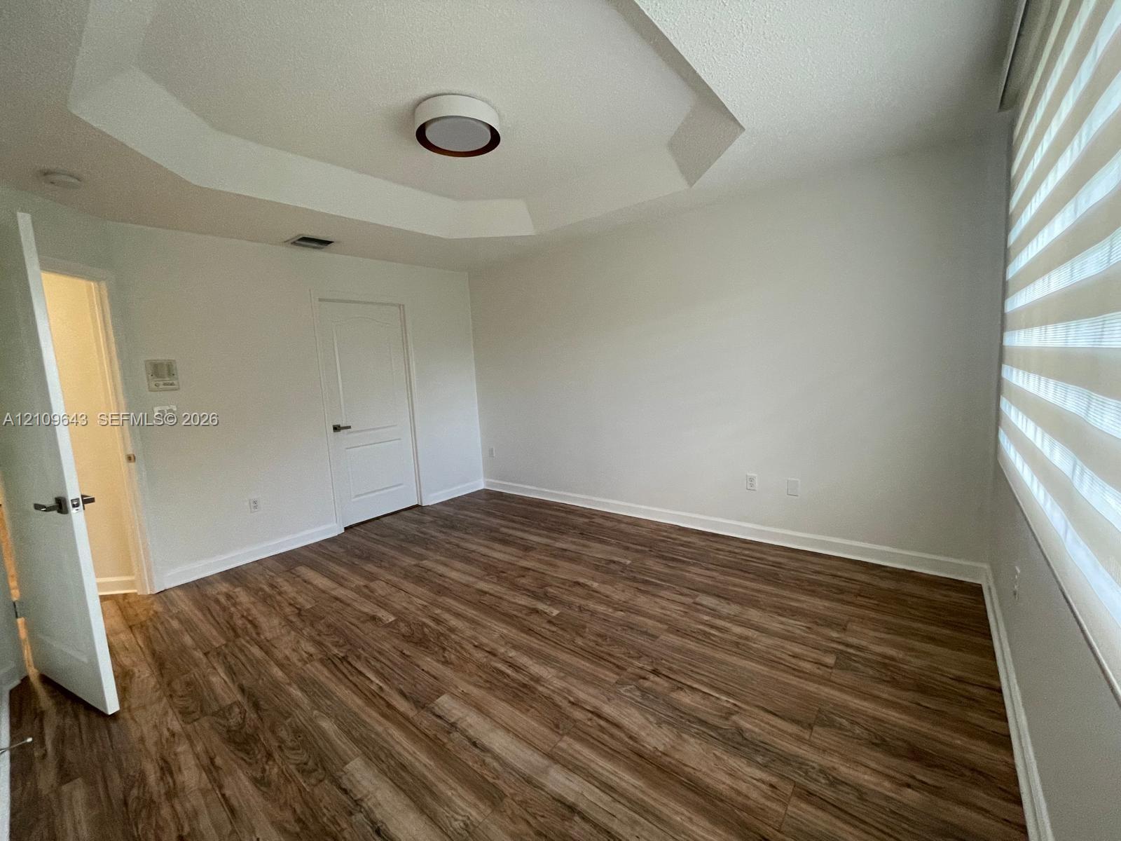 Room featuring tray ceiling, wood-finish flooring, paneled interior door, and window treatments