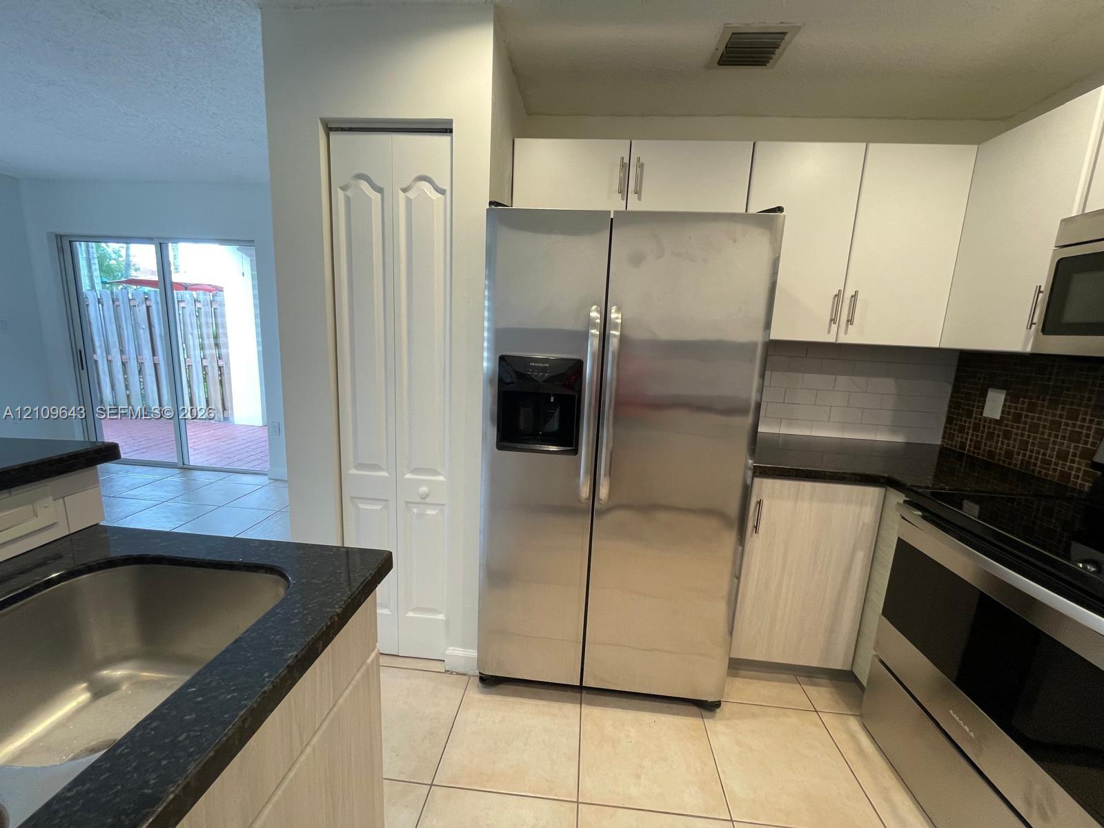 Kitchen featuring white cabinetry, dark countertops, a tile backsplash, stainless steel appliances, and tile flooring