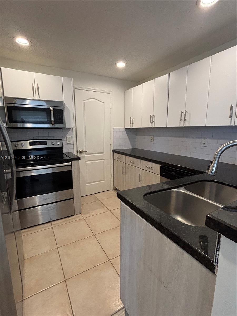 Kitchen featuring stainless steel appliances, dark stone-finish countertops, subway tile backsplash, recessed lighting, and white cabinetry