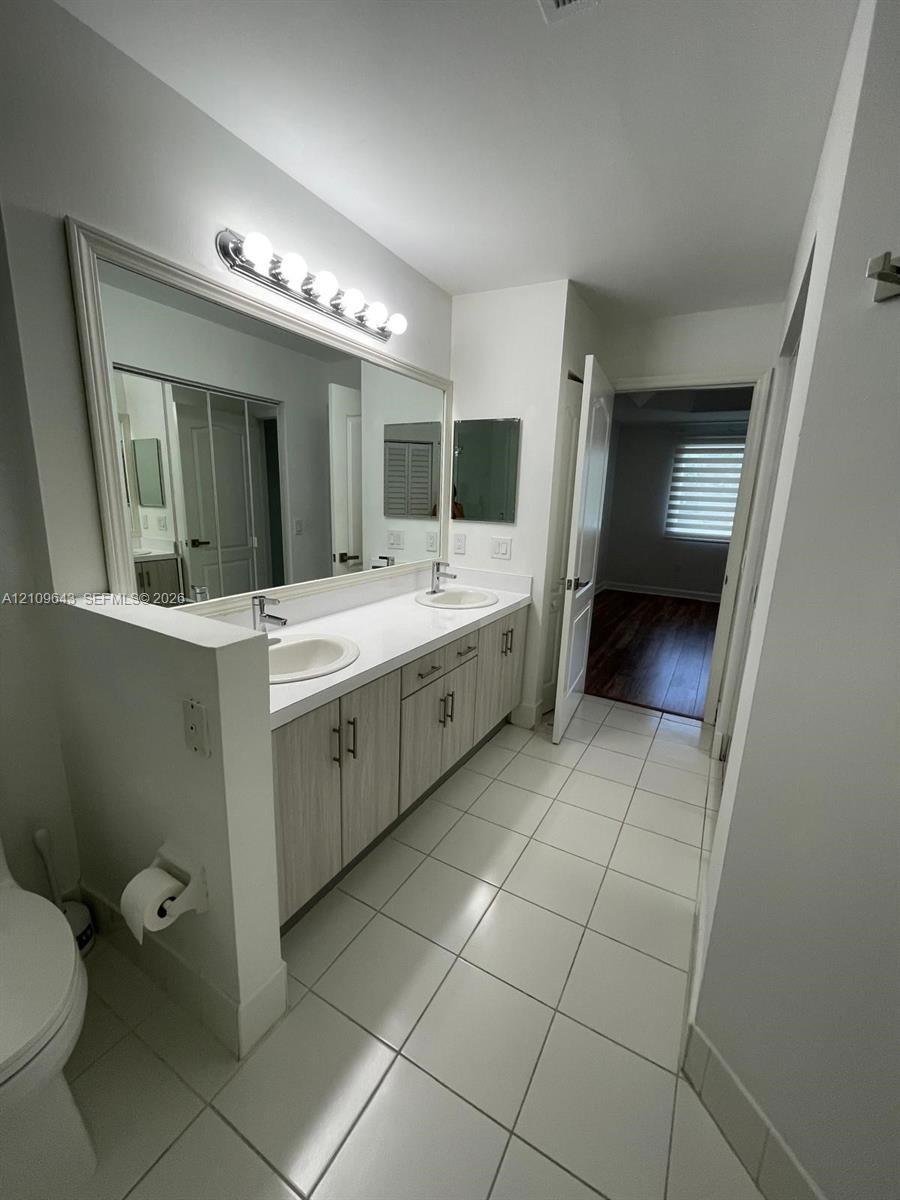 Double vanity featuring light-toned cabinetry, white countertop with dual drop-in sinks, full-width wall mirror, and large-format tile flooring