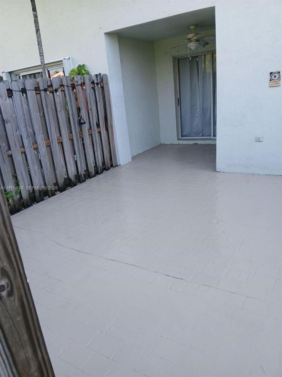 Covered concrete patio featuring a ceiling fan and vertical wood privacy fencing