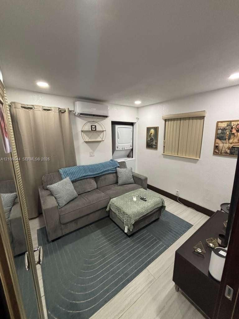 Interior space featuring recessed lighting, light-toned wood-finish flooring, a wall-mounted ductless mini-split system, and a built-in stackable laundry unit Interior space featuring recessed lighting, light-toned wood-finish flooring, a wall-mounted ductless mini-split system, and a built-in stackable laundry unit