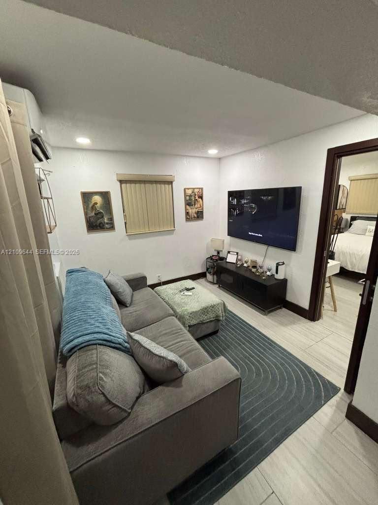 Neutral-toned room featuring recessed ceiling lighting, light-colored tile flooring, and a wall-mounted ductless climate control unit Neutral-toned room featuring recessed ceiling lighting, light-colored tile flooring, and a wall-mounted ductless climate control unit