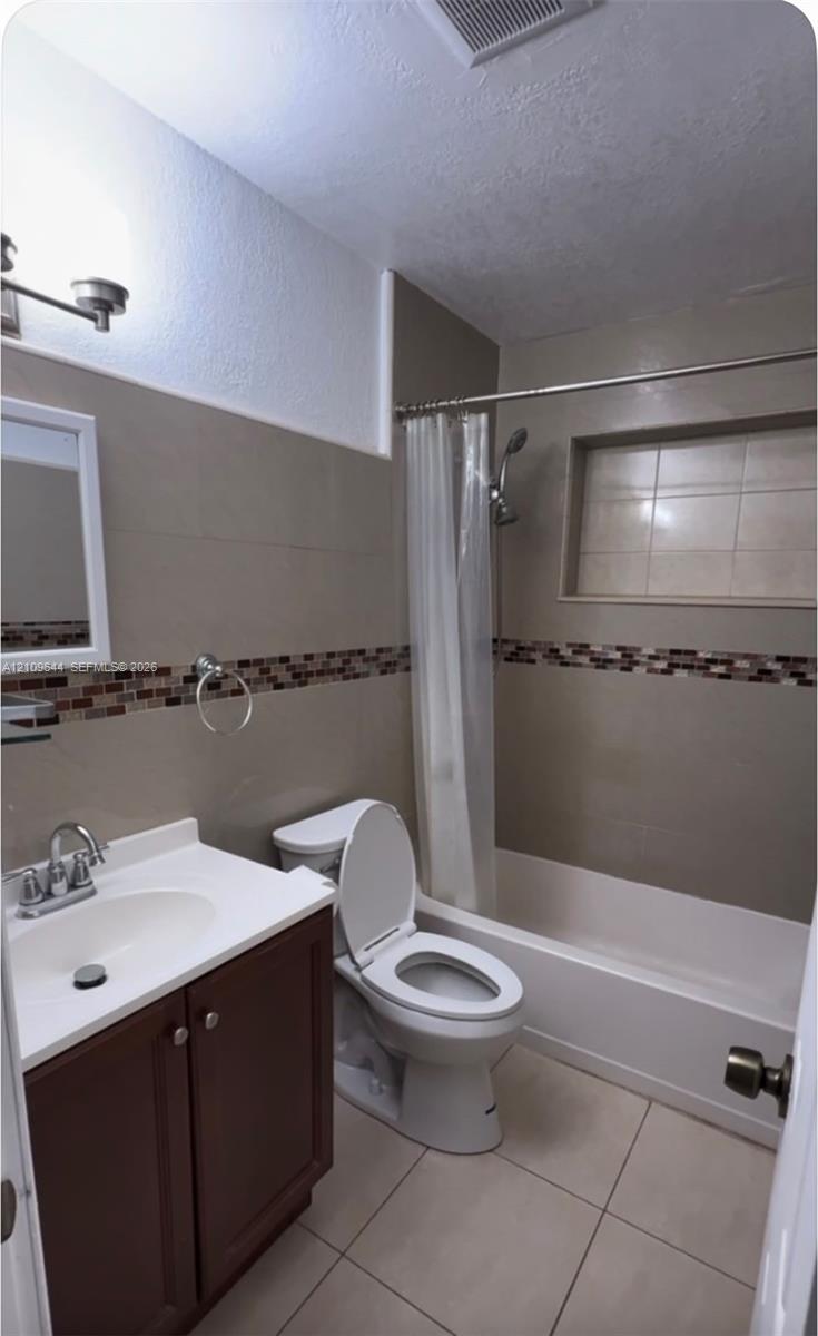 Bathroom featuring tile flooring, vanity with white countertop, integrated shower niche, and decorative mosaic tile backsplash Bathroom featuring tile flooring, vanity with white countertop, integrated shower niche, and decorative mosaic tile backsplash
