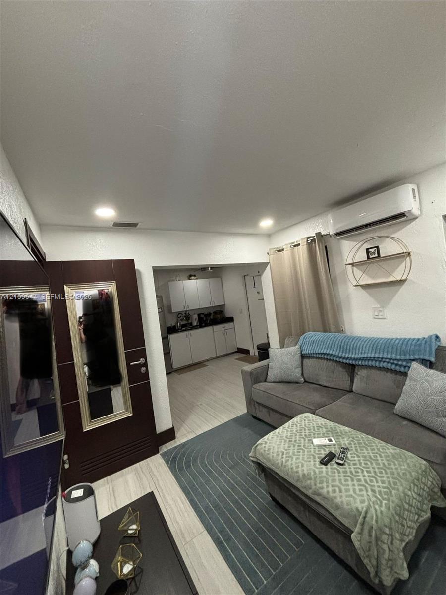 Living space featuring wood-finish flooring, recessed lighting, wall-mounted ductless air conditioning unit, and a dark-toned interior door with integrated mirror Living space featuring wood-finish flooring, recessed lighting, wall-mounted ductless air conditioning unit, and a dark-toned interior door with integrated mirror