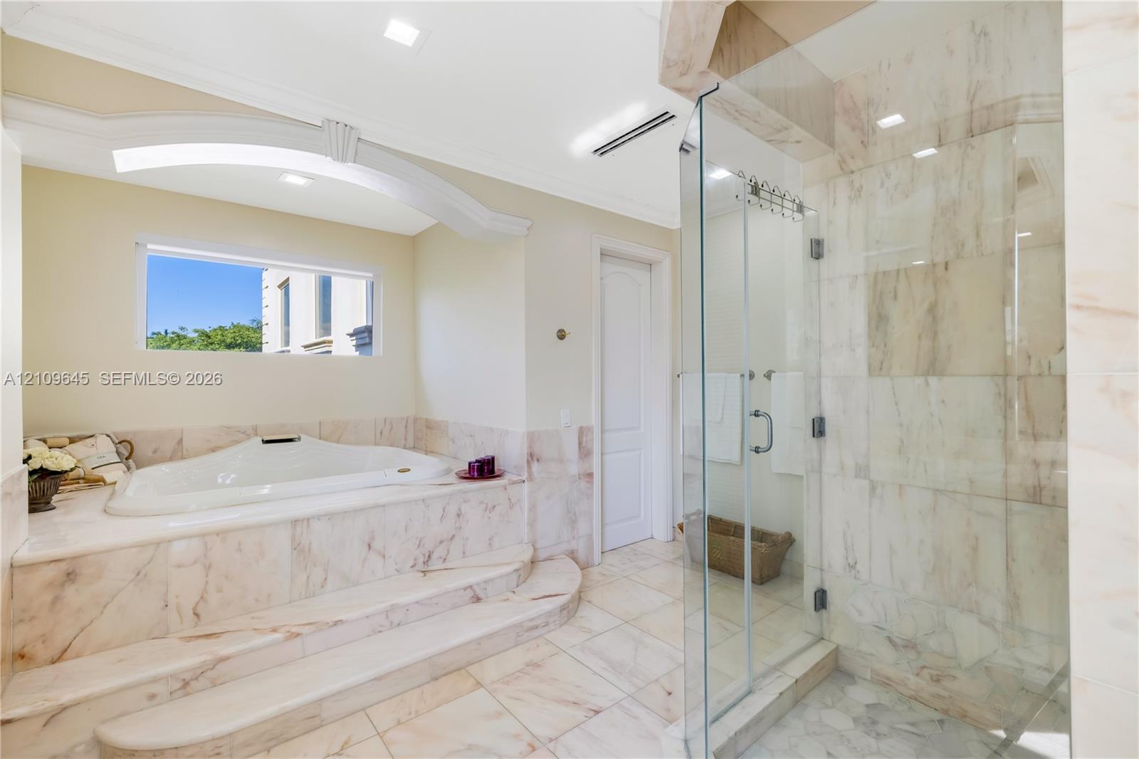 Jetted soaking tub with a stepped stone surround, walk-in shower with glass enclosure, stone tile flooring, and recessed ceiling lighting