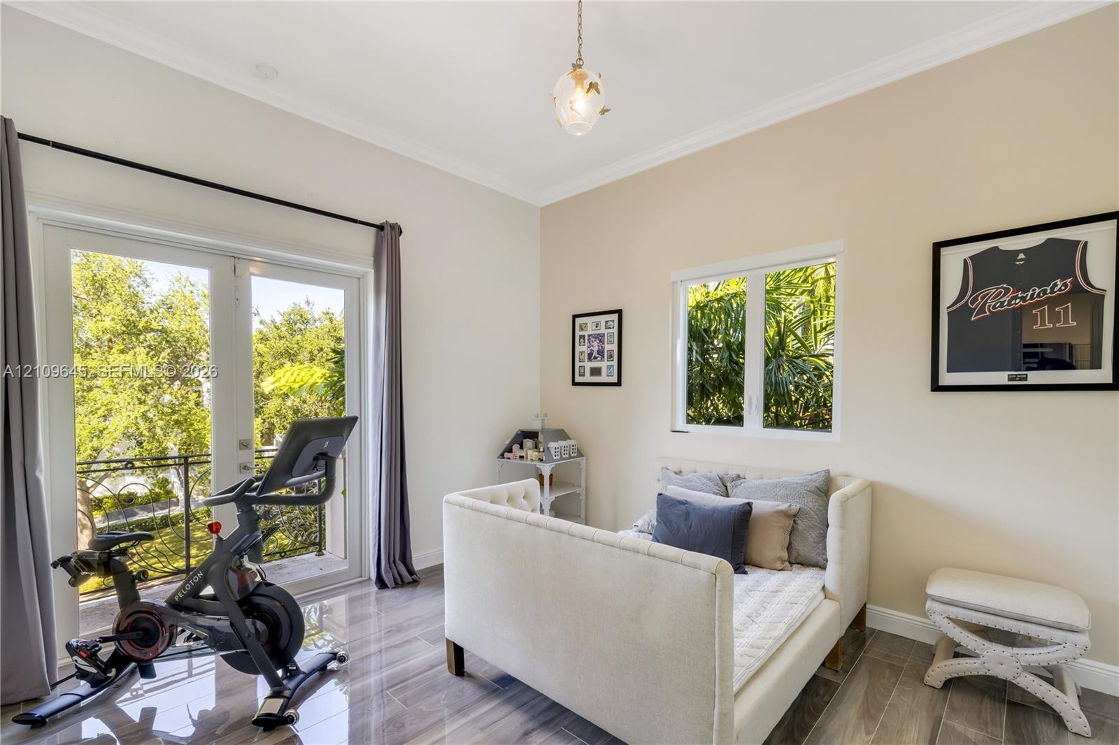 Room featuring wood-finish tile flooring, crown molding, glass-paned French doors opening to a balcony with decorative railing, and a pendant light fixture